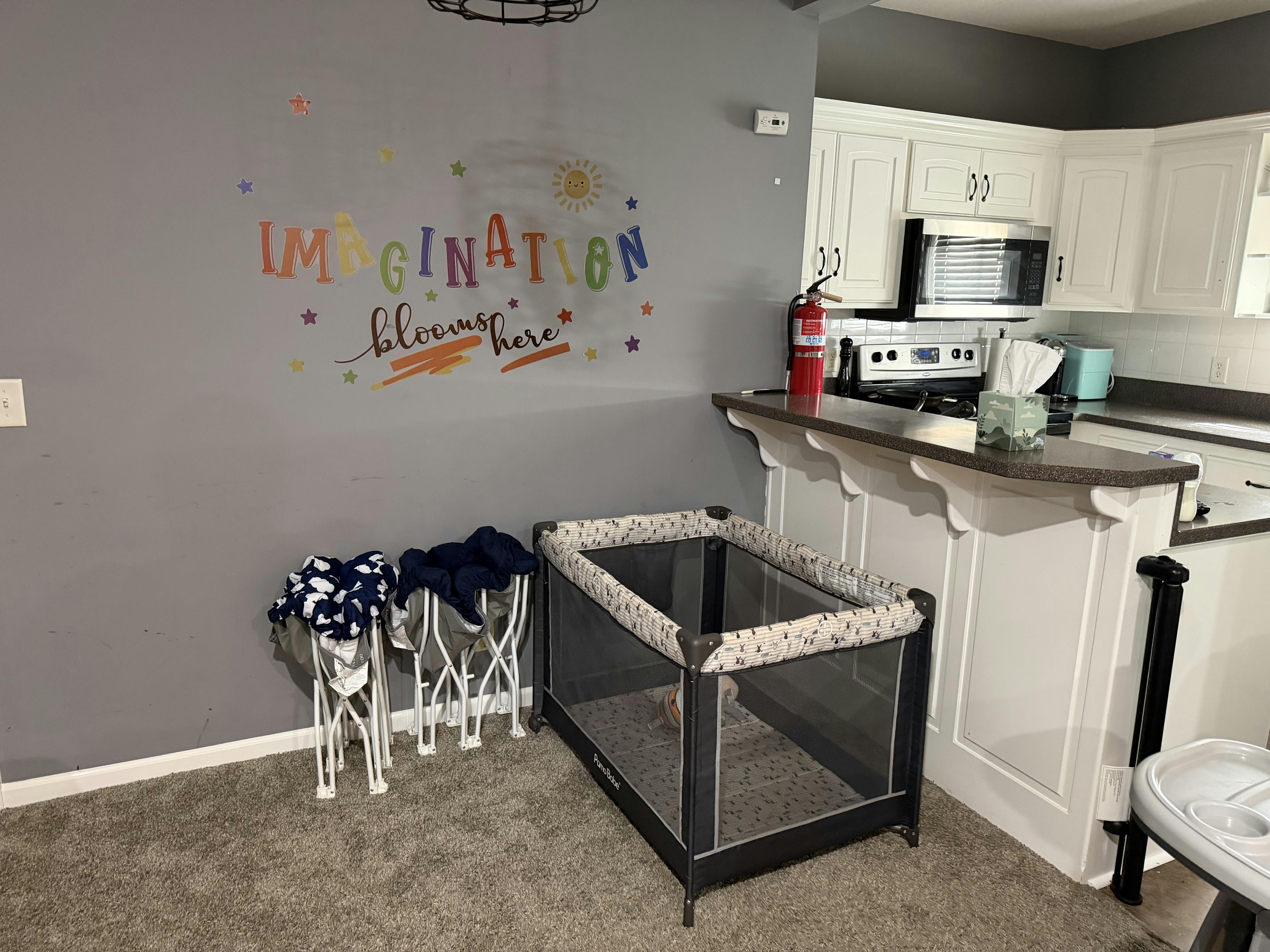 Playard and folded chairs in front of a wall with 'Imagination blooms here' decal