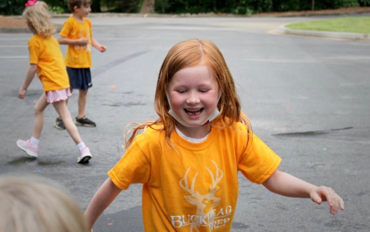Child in yellow shirt with eyes closed, smiling, with other children in background
