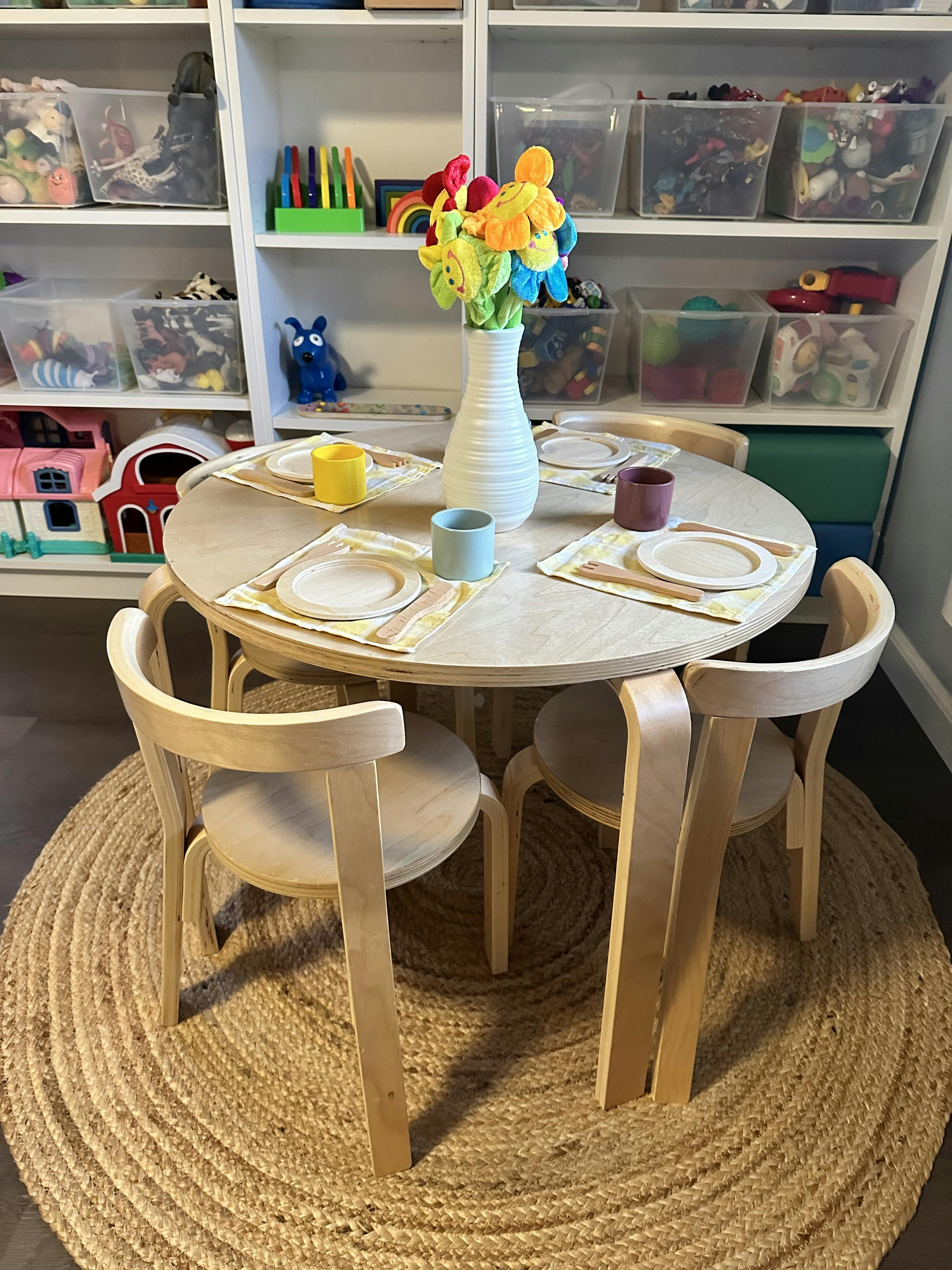 Small wooden table set for children with toy dishes and a vase of fabric flowers