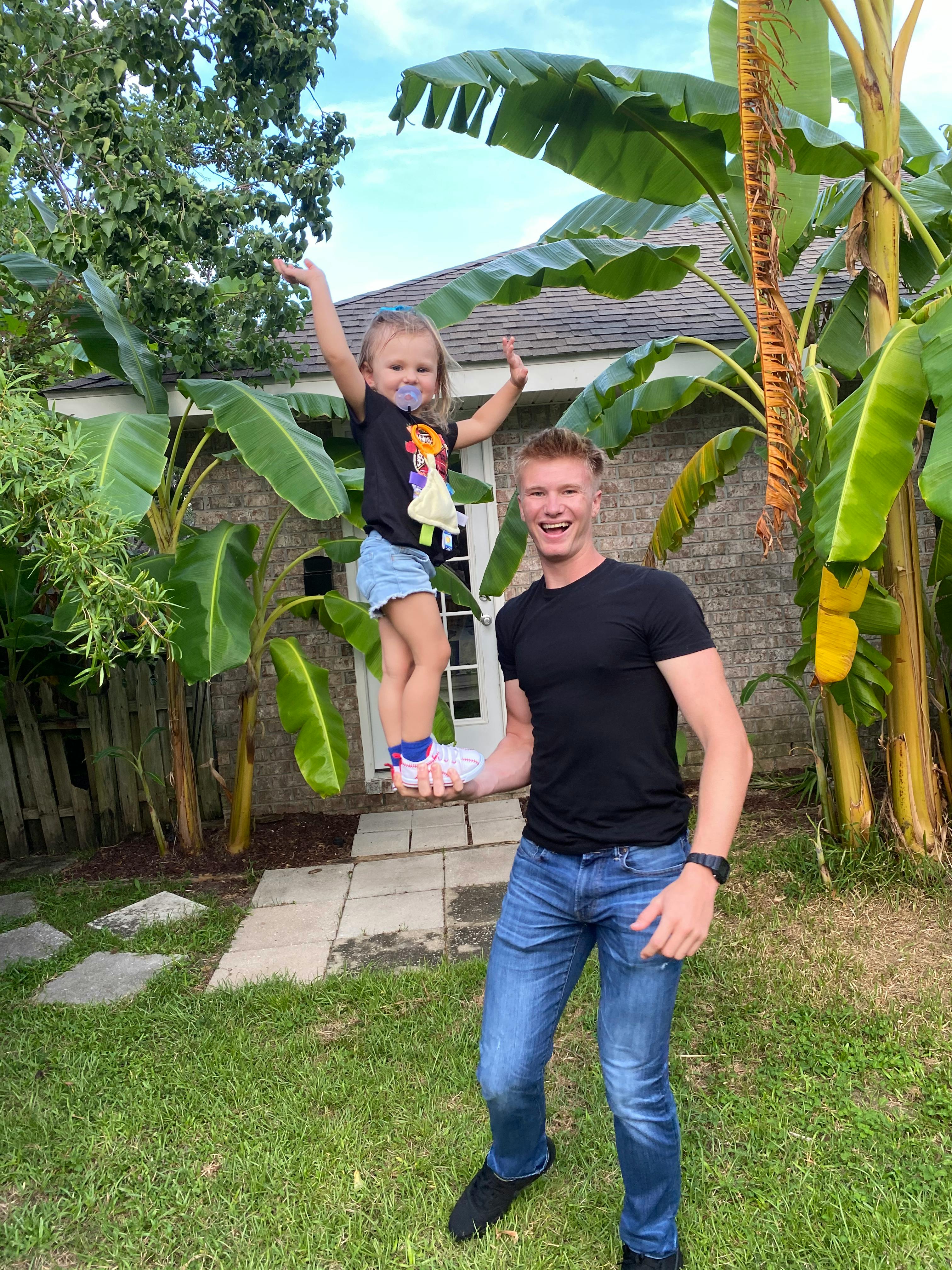Person holding a child up by one hand in a yard