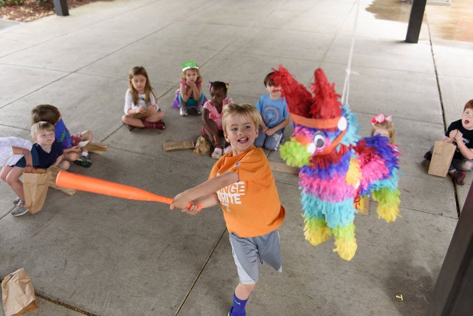 Child swinging a bat at a colorful piñata with other children watching