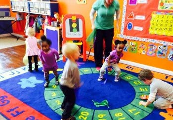 Adult and children playing on a rug with numbers in a classroom