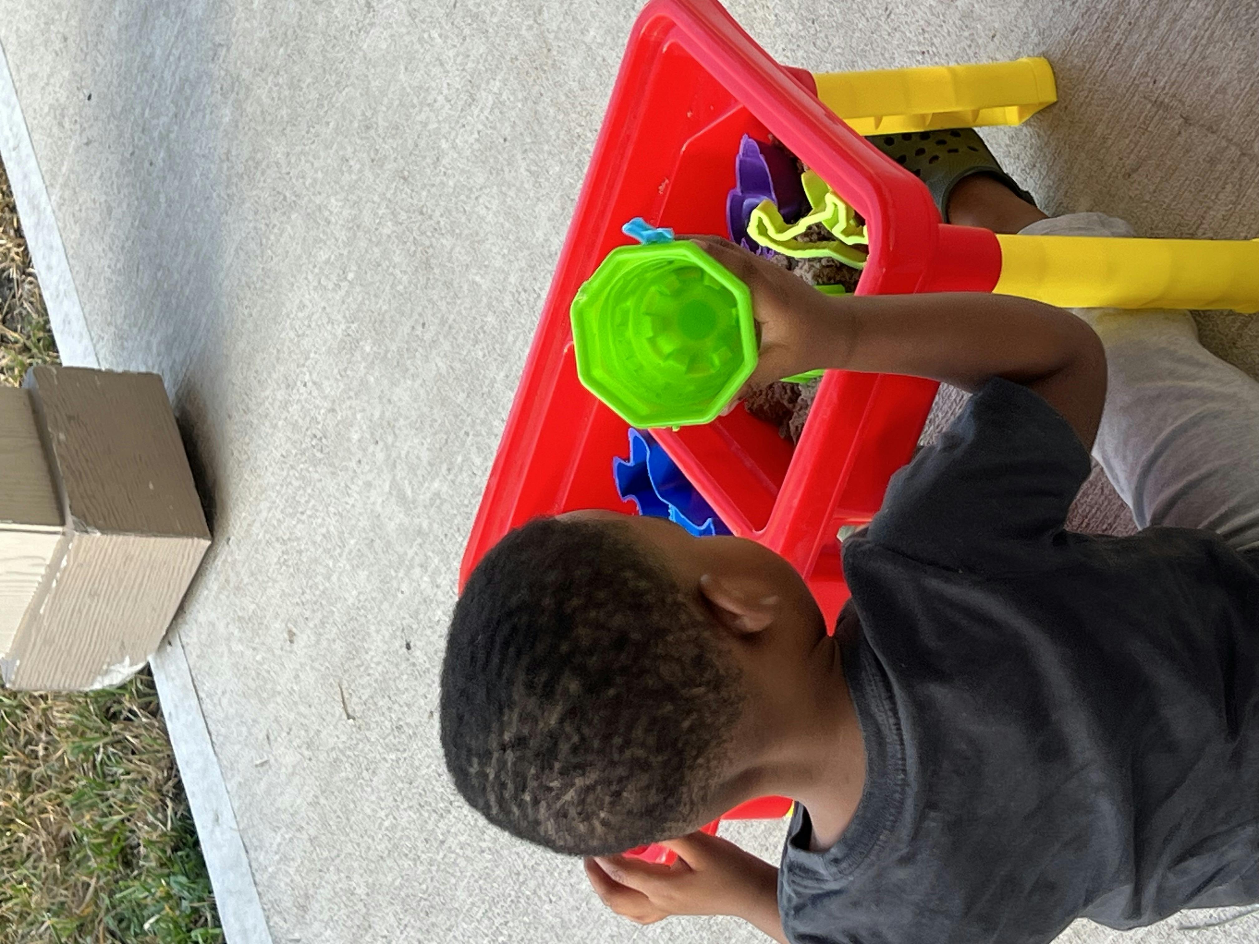 Child playing with a green toy cup over a red toy