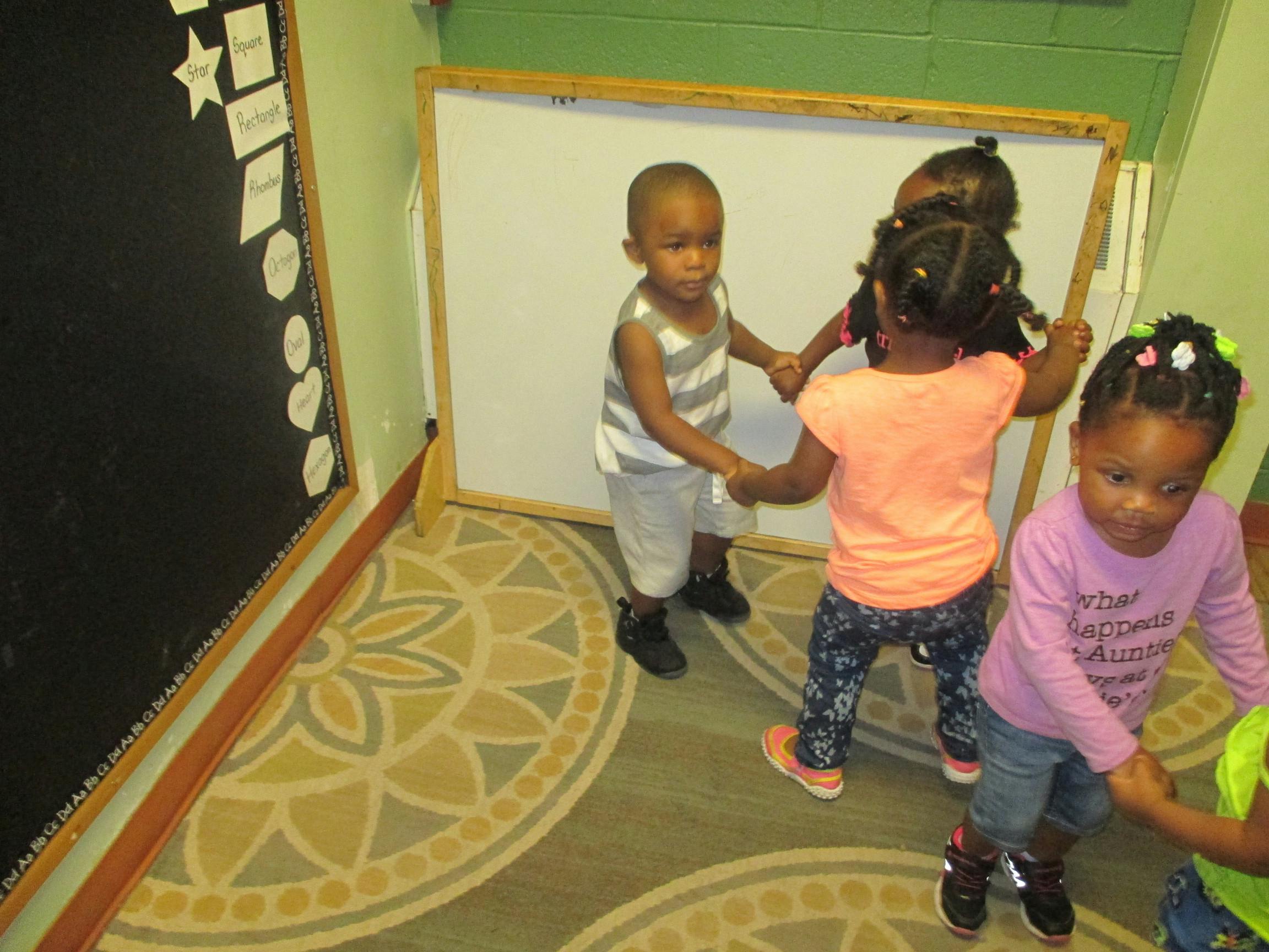 Four children holding hands in a circle in a classroom