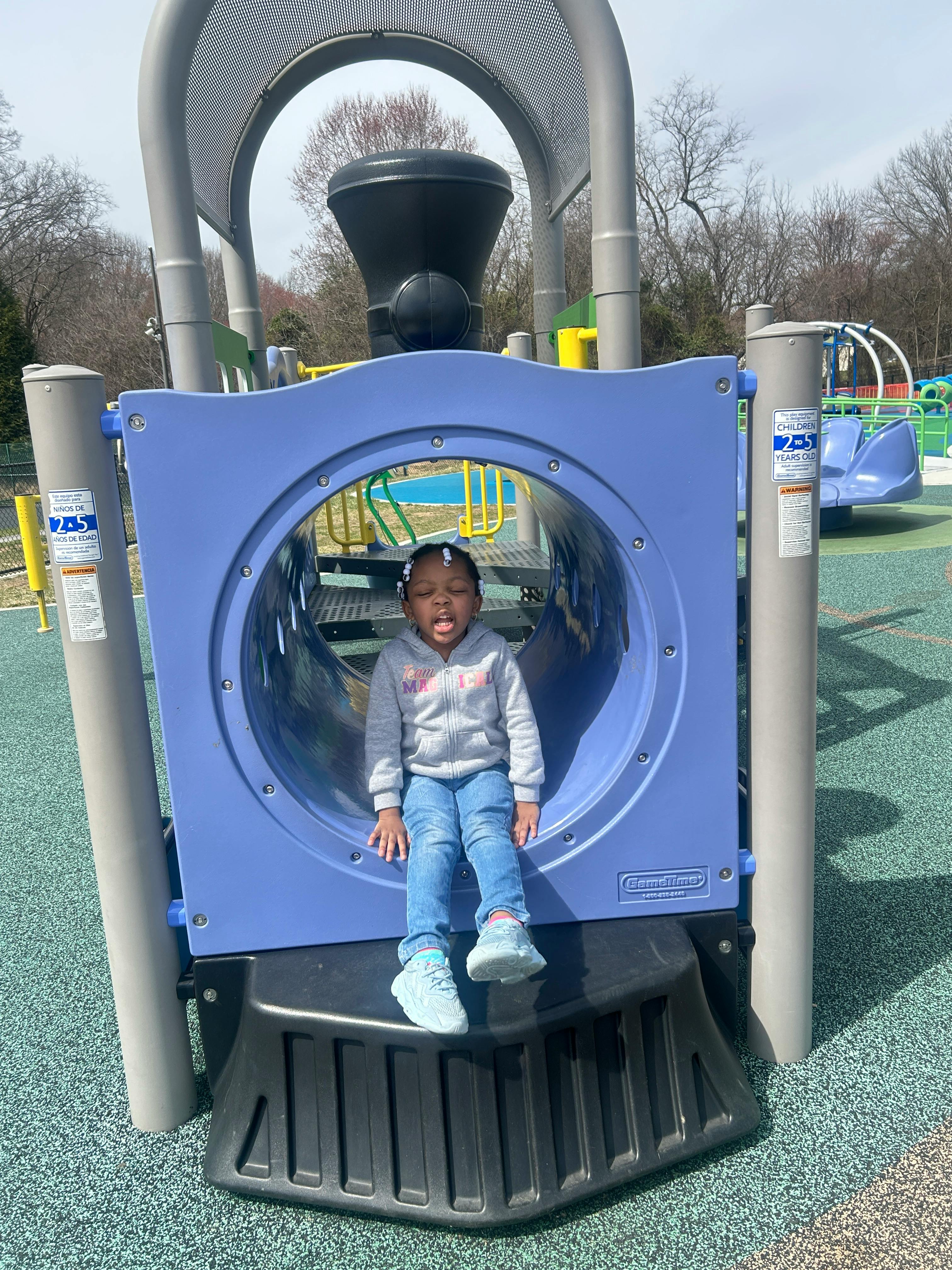 Child sitting in a blue play tunnel on a playground
