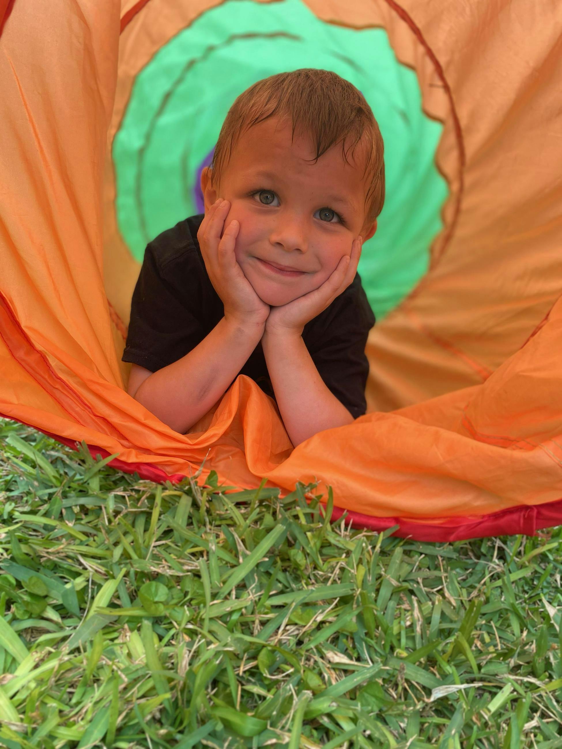 Child in a play tunnel with hands under chin