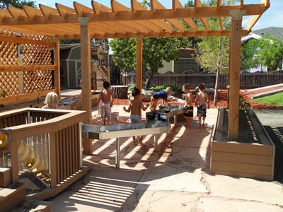 Children playing at water tables under a wooden pergola
