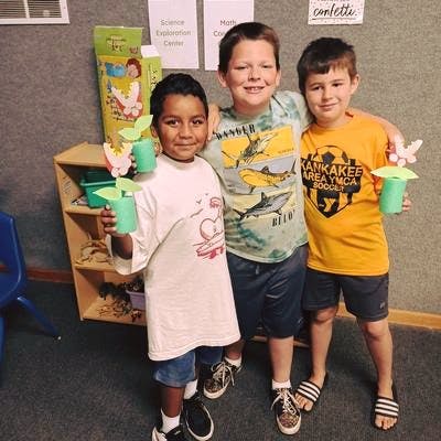Three children holding crafts, one with arm around another