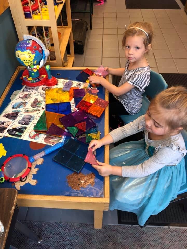Two children playing with colorful magnetic tiles at a table