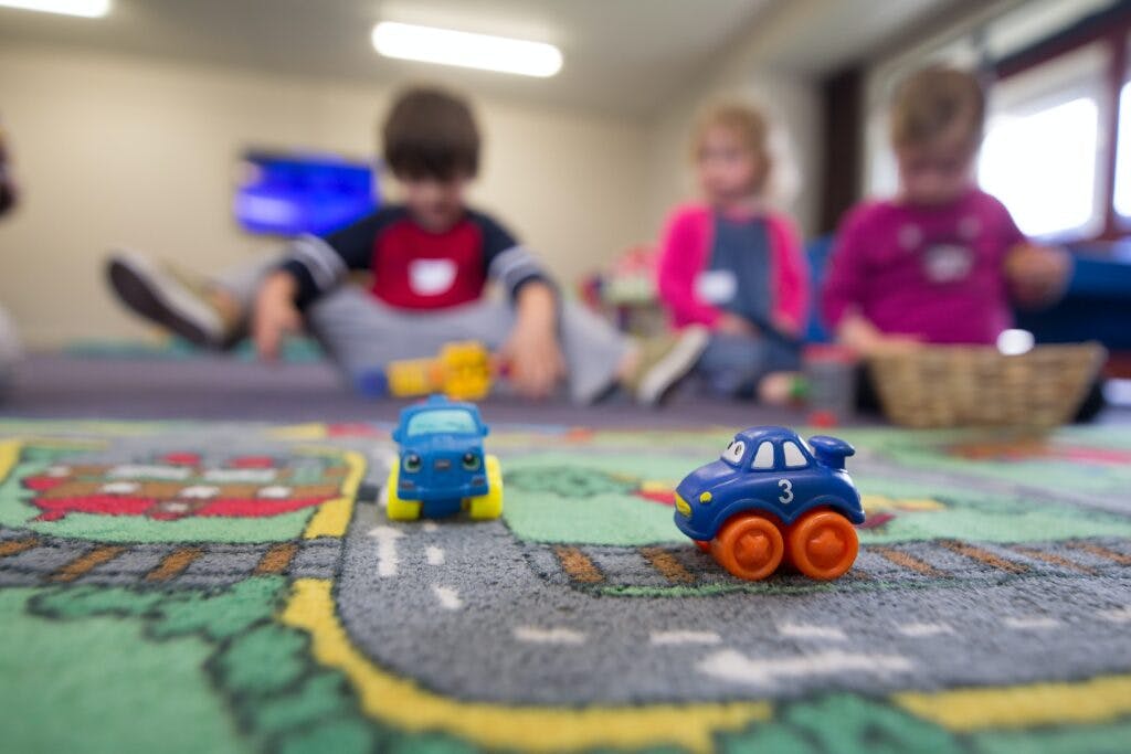Toy cars on a playmat with children in the background