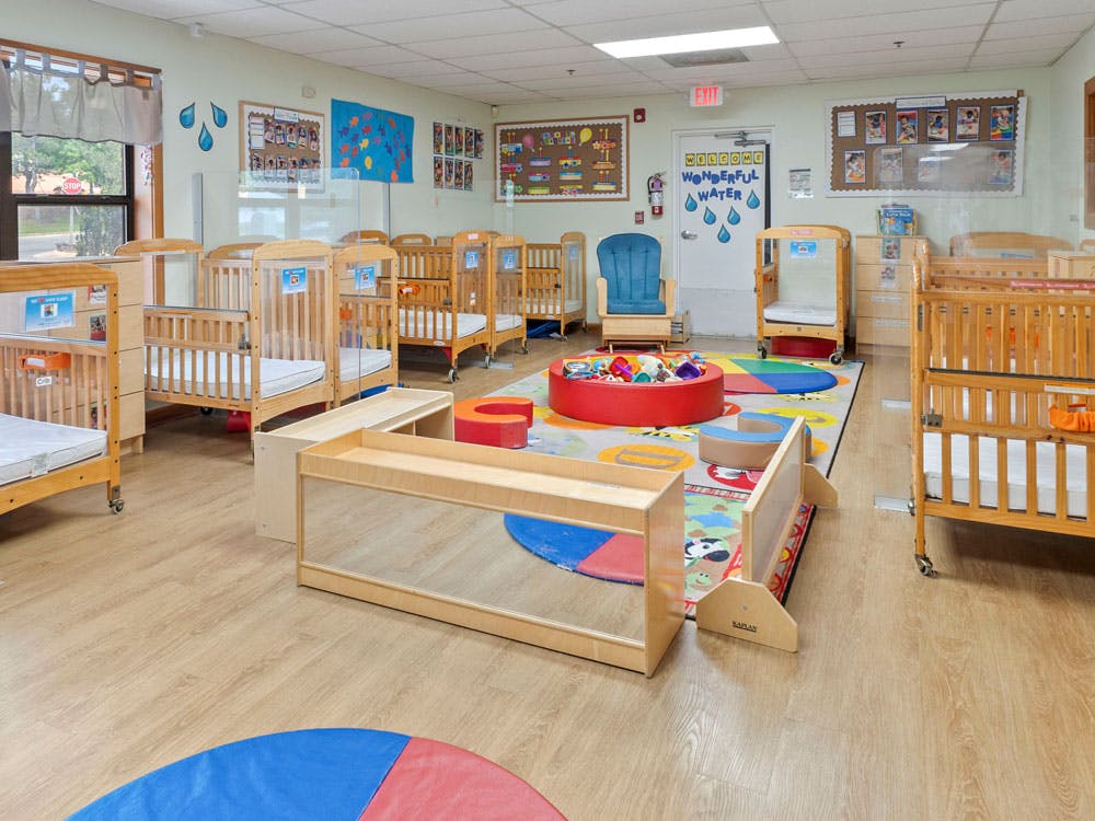 A room with multiple cribs, a colorful rug, and child-sized furniture