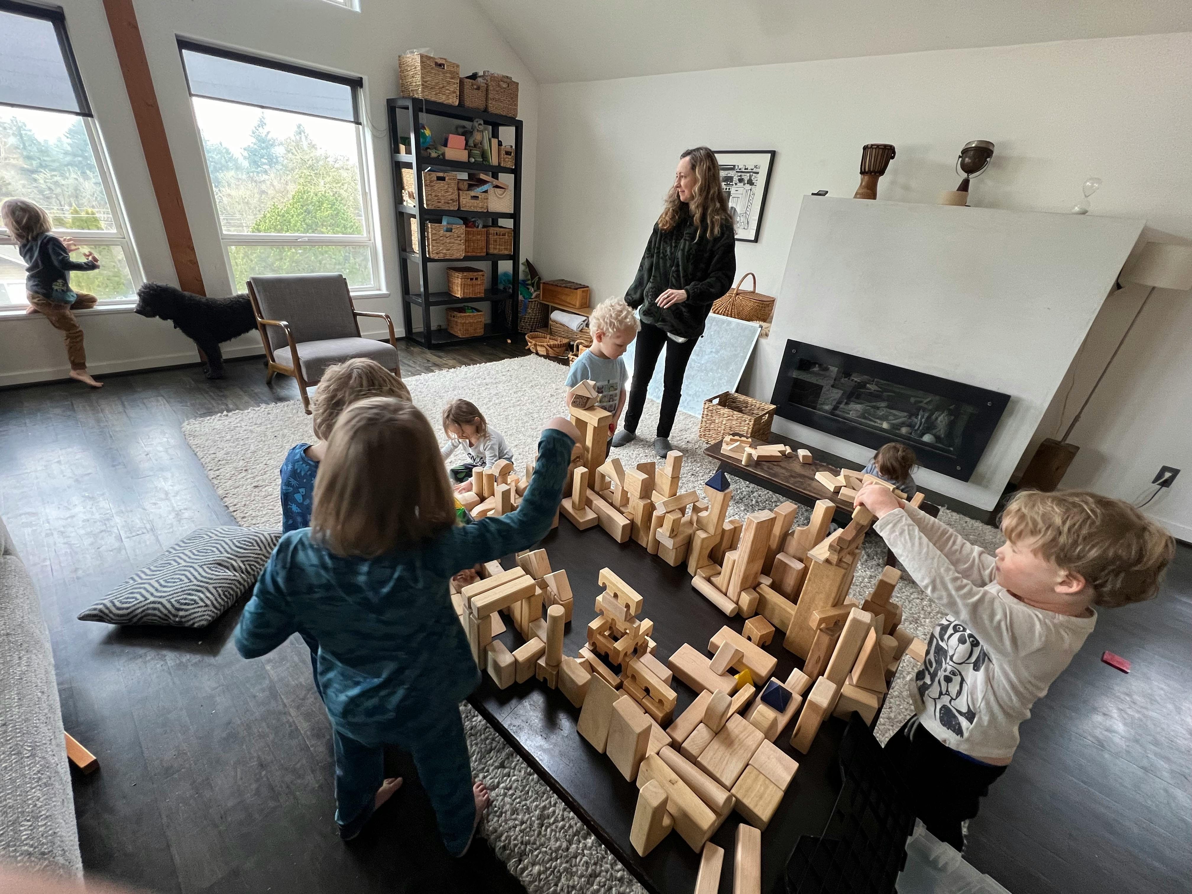 Children playing with wooden blocks in a room with an adult supervising