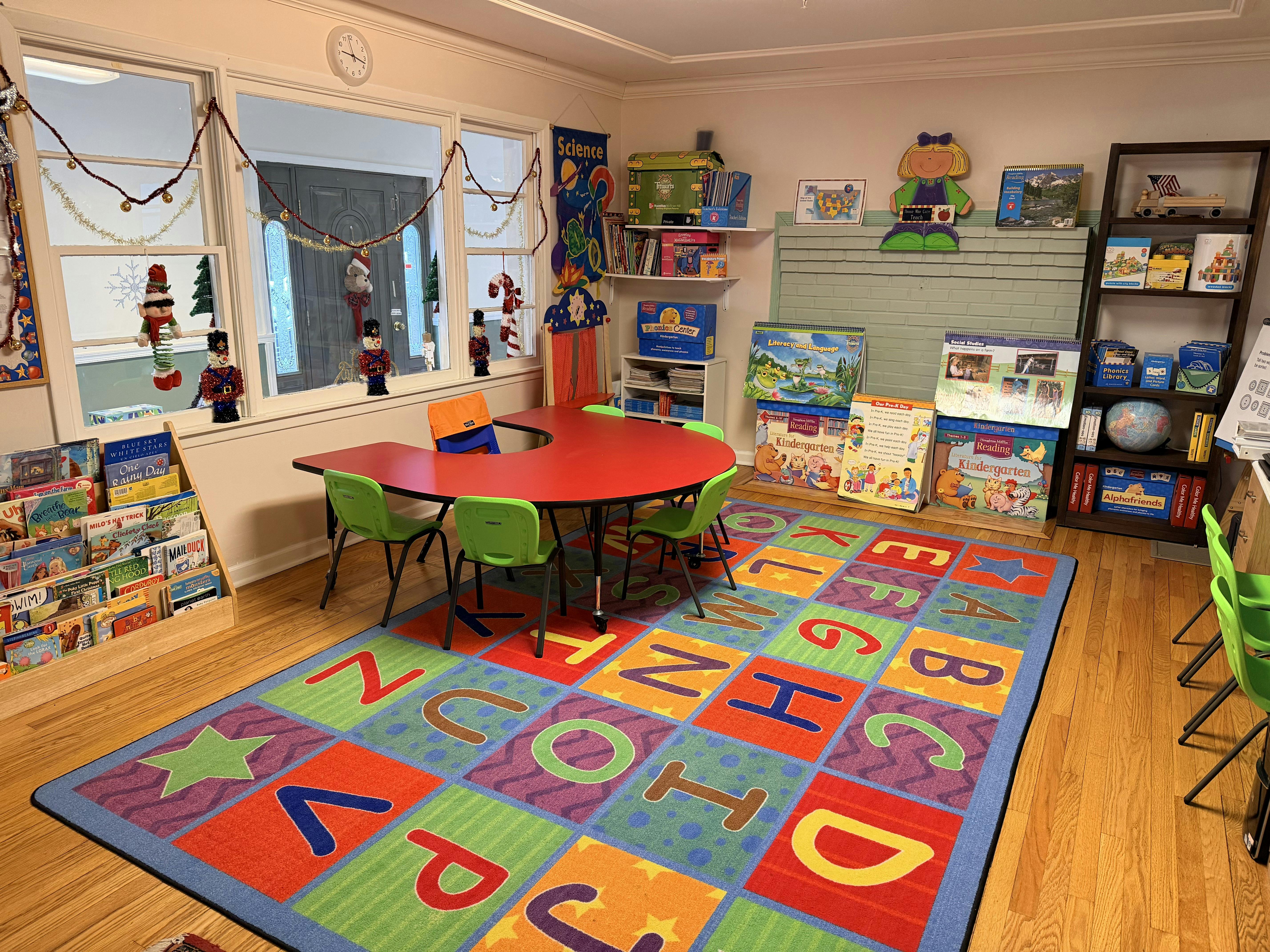 Classroom with a red U-shaped table and green chairs on an alphabet rug