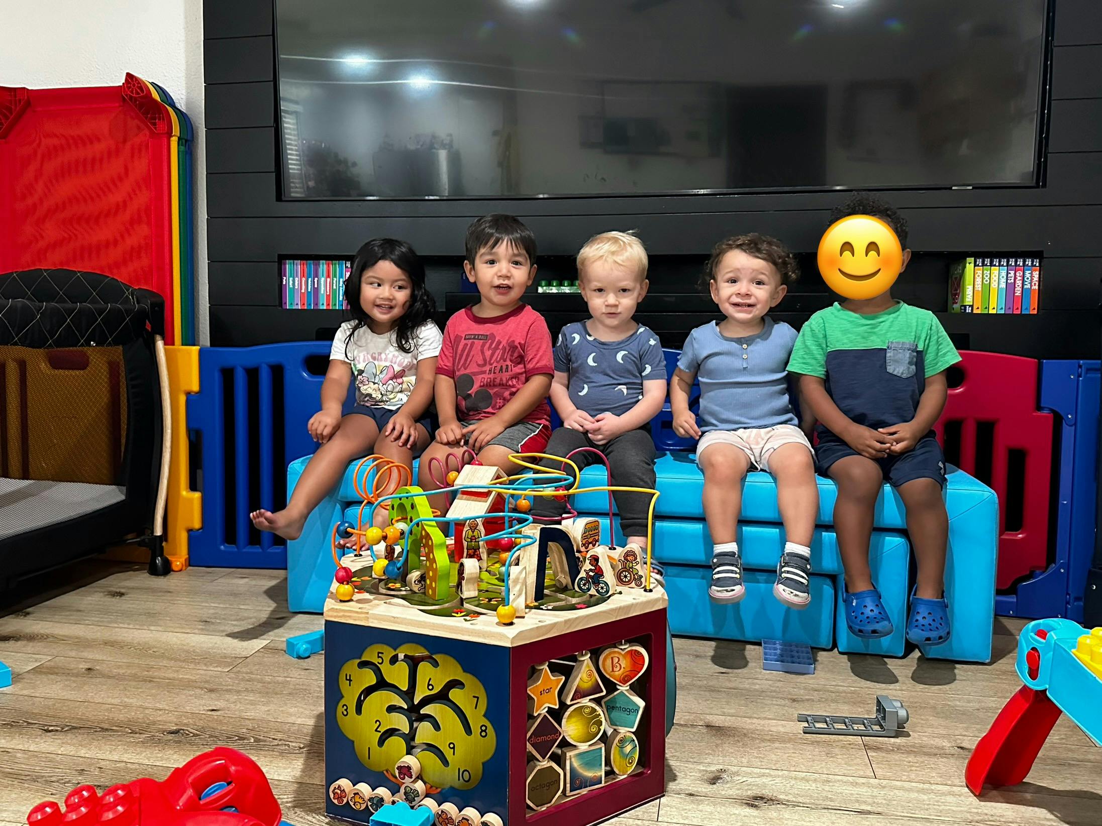 Four children sitting on a blue bench with a play cube in front