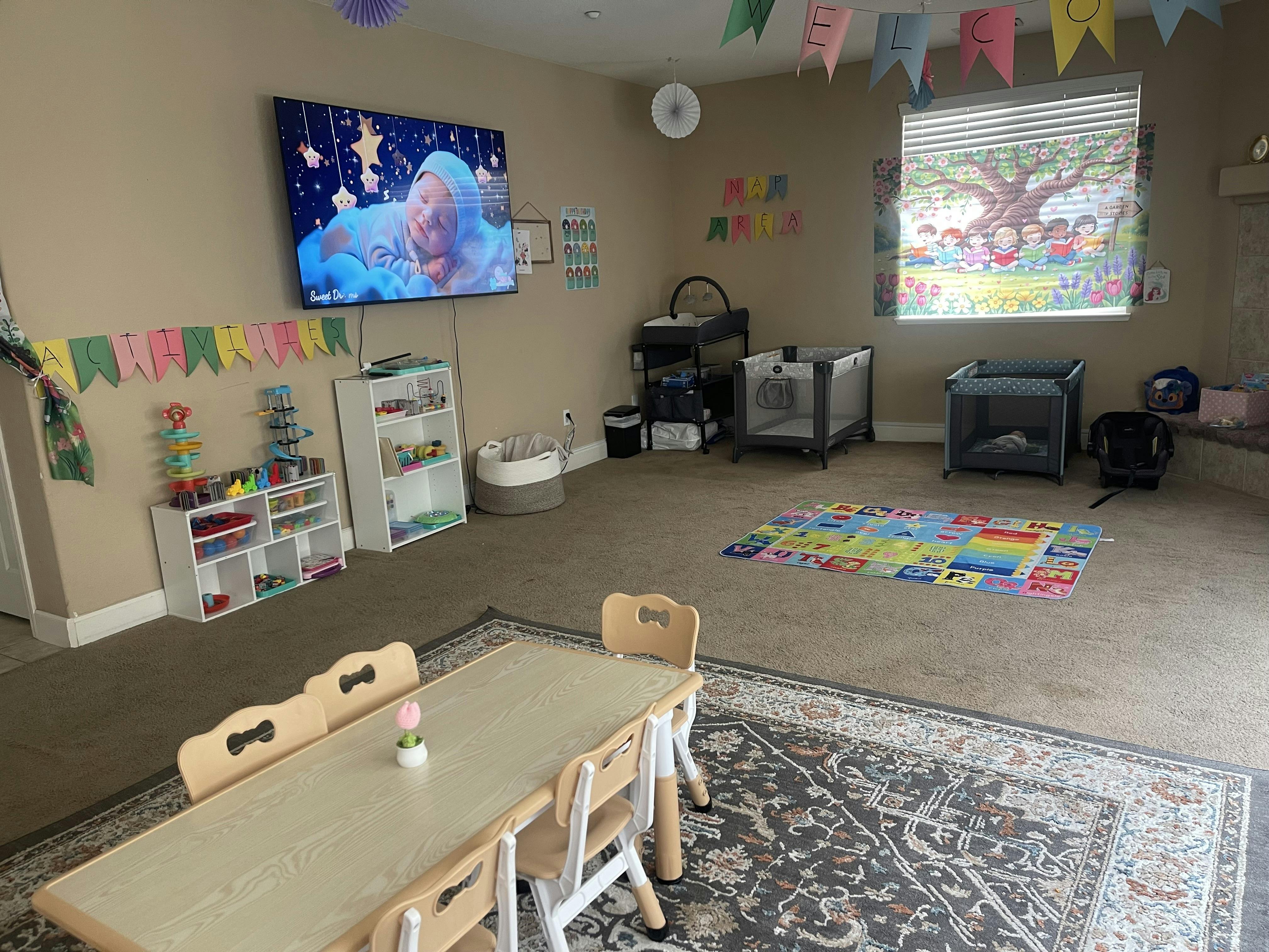 Playroom with small tables and chairs, play mats, shelving with toys, and a TV