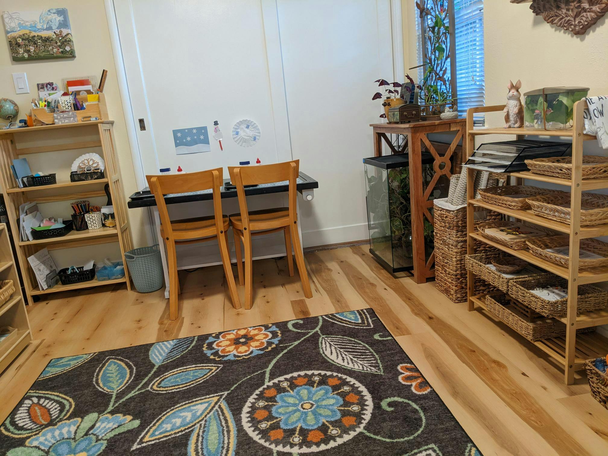Two wooden chairs at a table in a room with shelves and a patterned rug