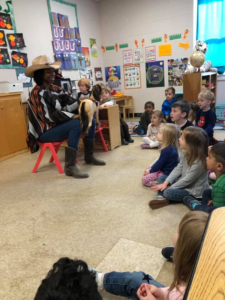 Person in a hat holding a goat for children in a classroom