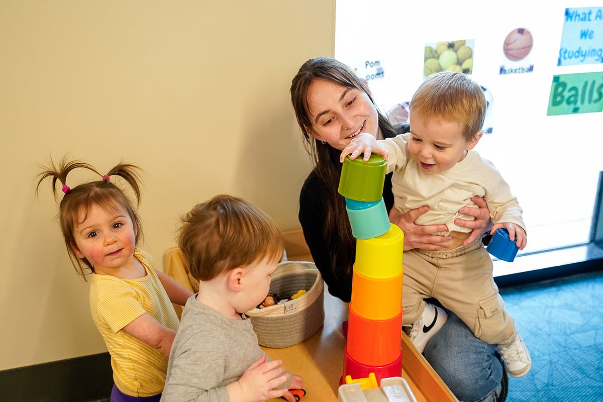 Person holding a child who is stacking colorful cups, with two other children nearby