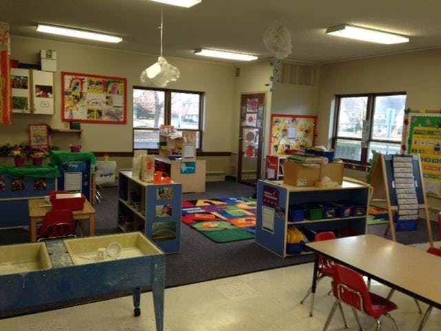 An empty classroom with child-sized tables, chairs, and learning materials