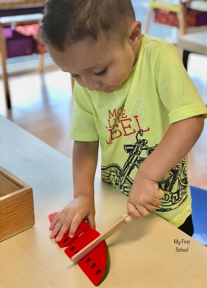 Child cutting a toy watermelon with a wooden knife