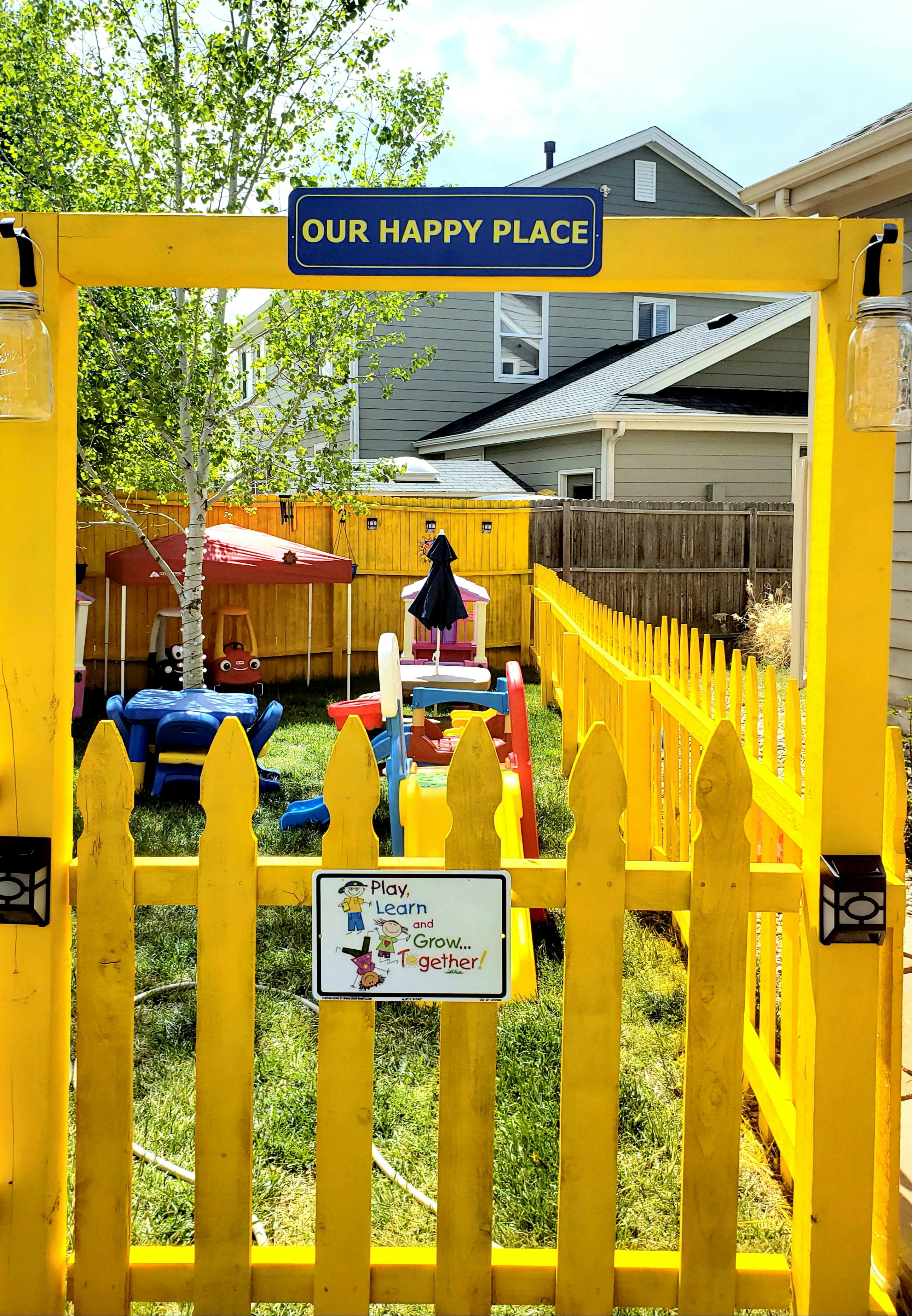 Yellow fence and gate with a sign that says "Our Happy Place"