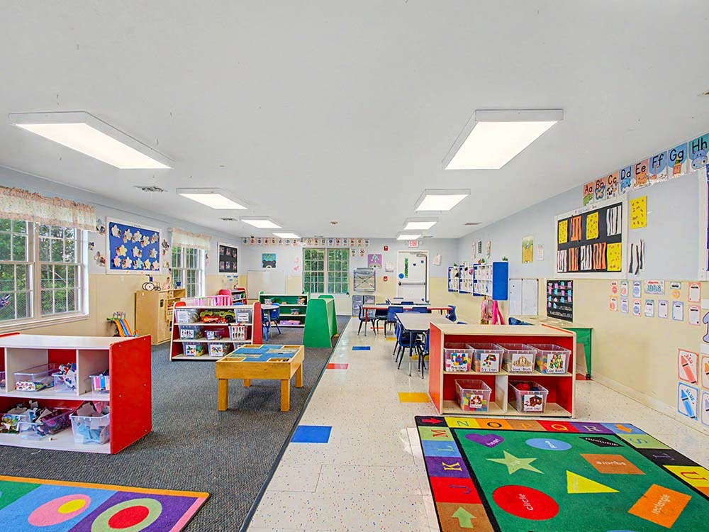 An empty early childhood classroom with colorful rugs, shelves, and tables