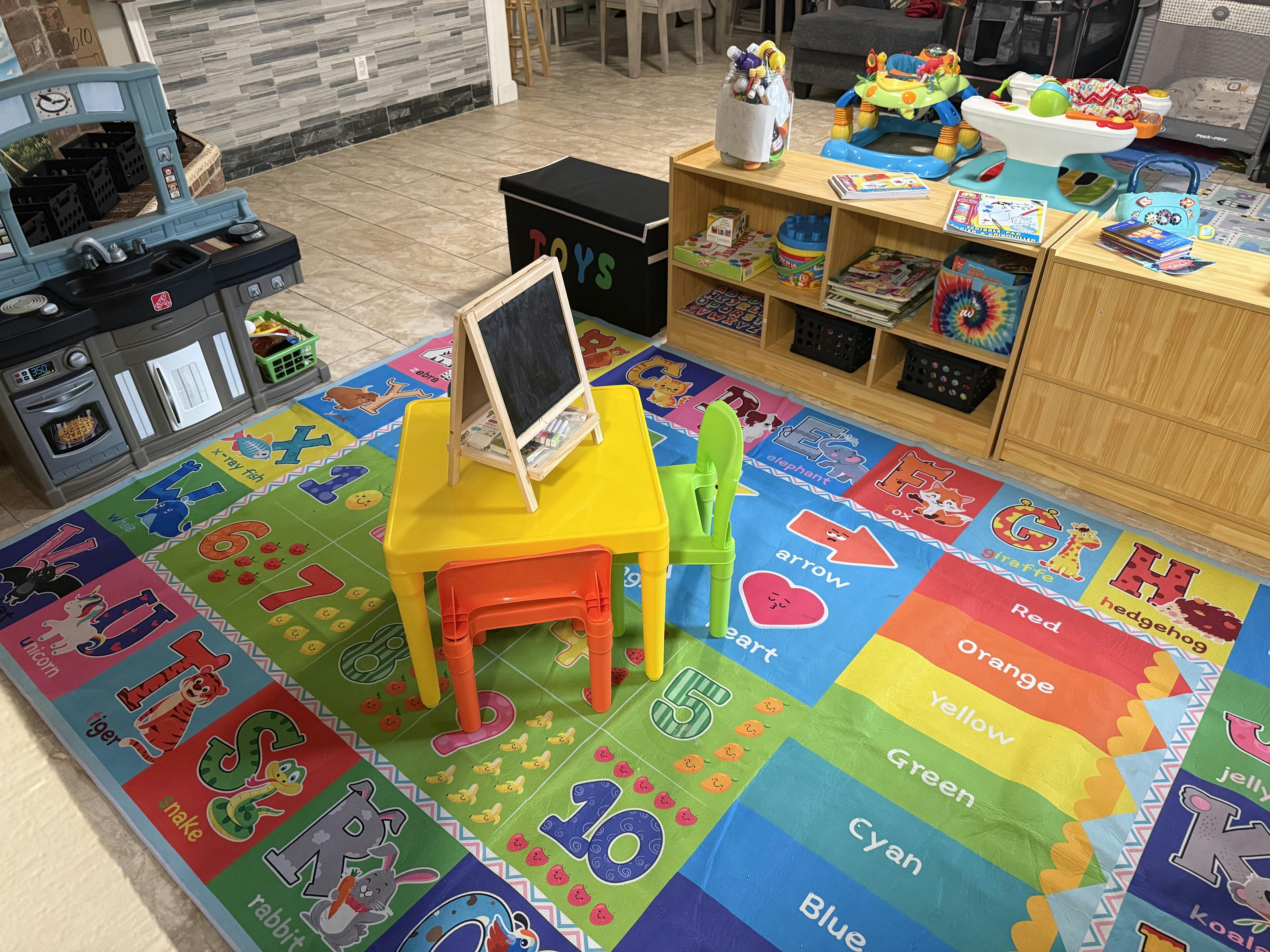 Colorful playroom with an alphabet rug, a play kitchen, and a small table with a chalkboard