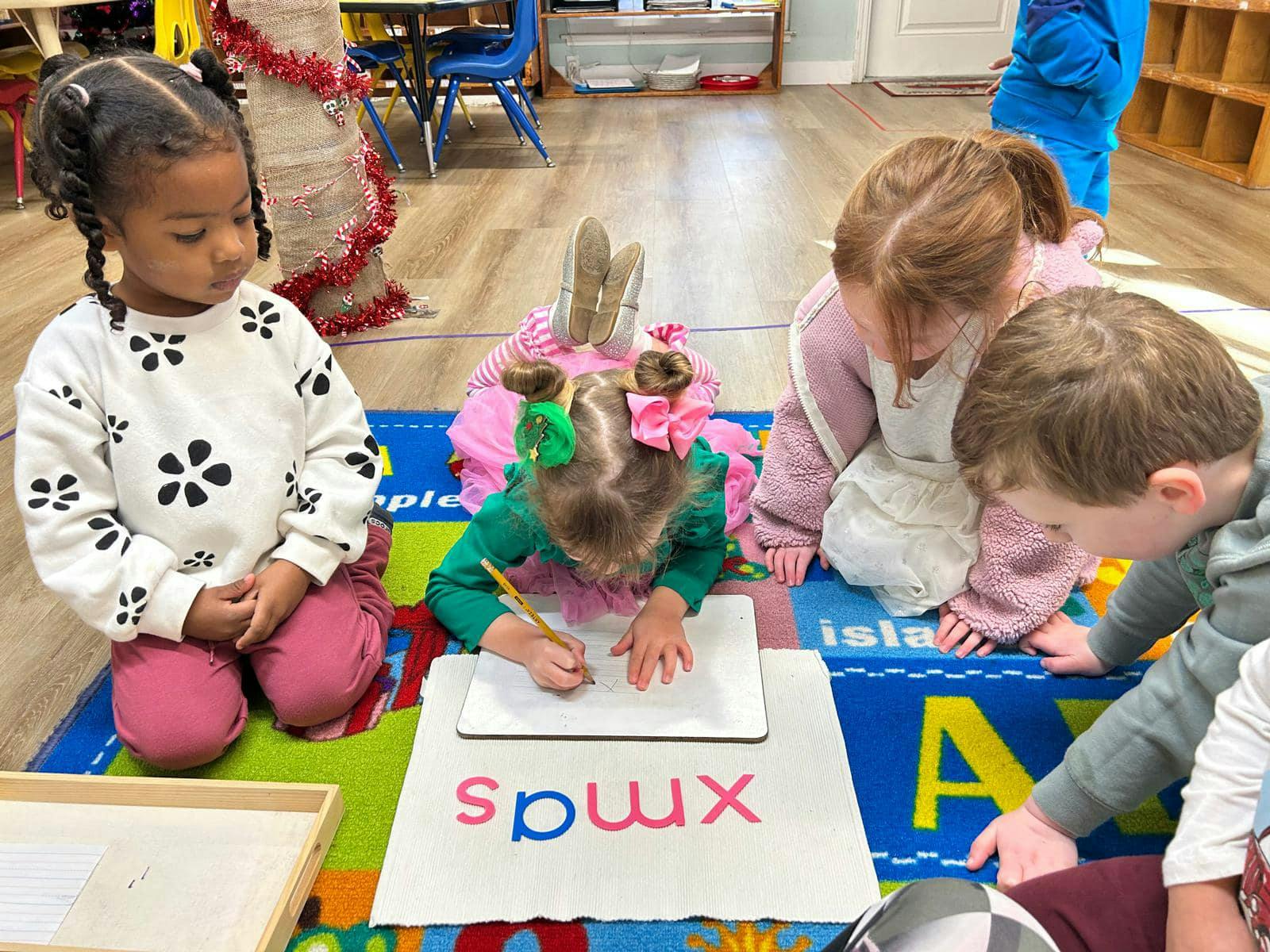 Four children on a rug, one writing on paper with a pencil