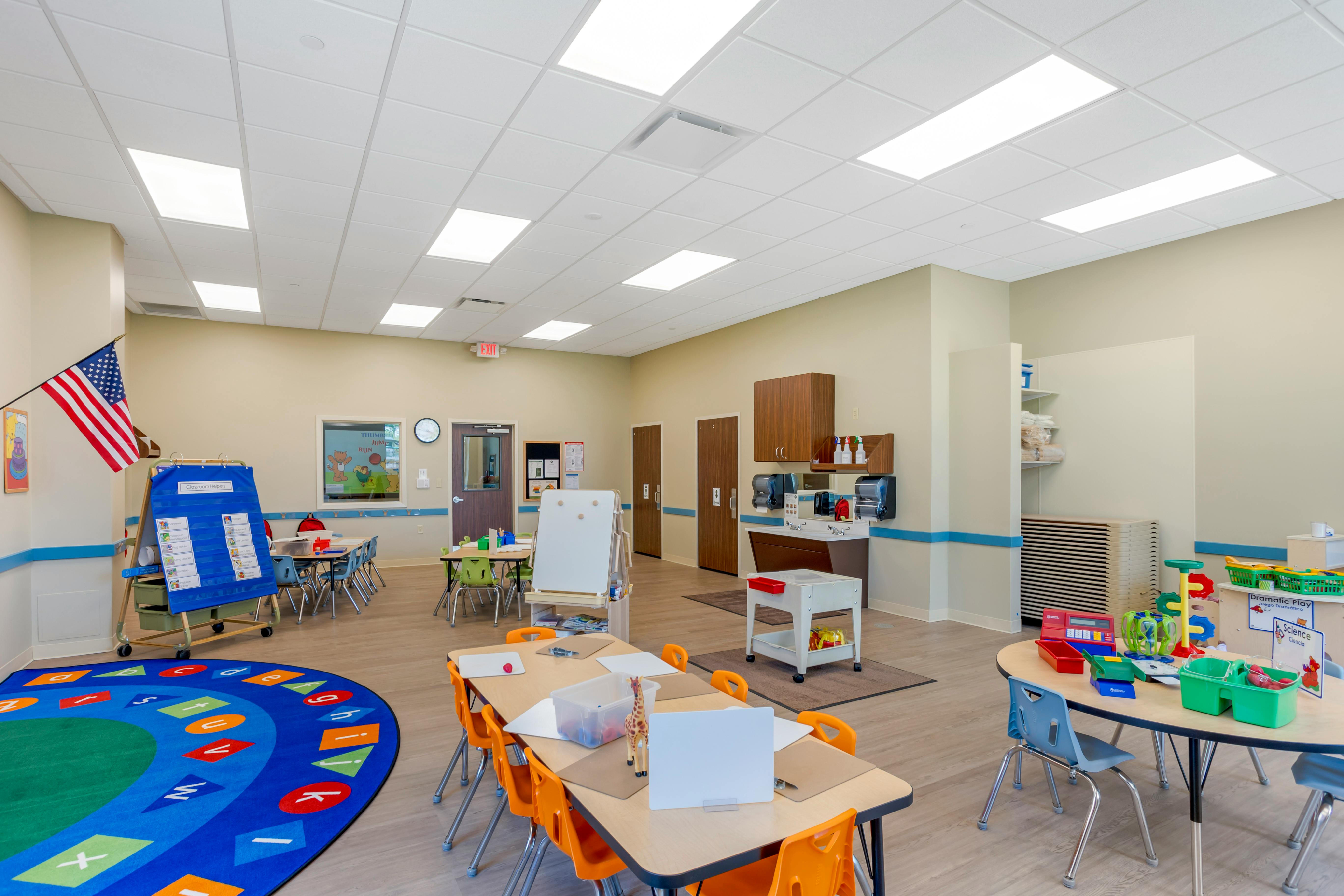 An empty classroom with multiple tables, chairs, and play areas