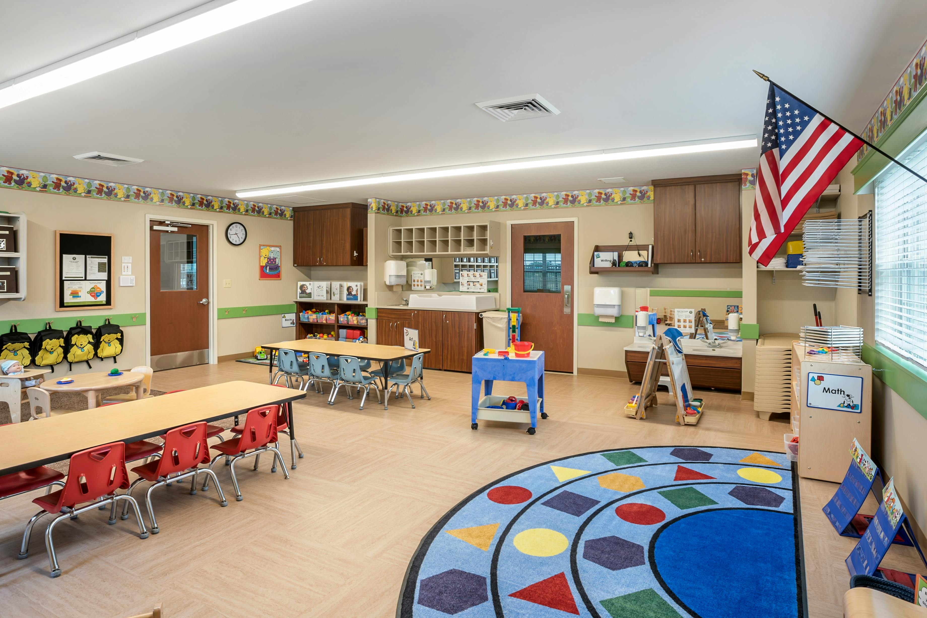 An empty preschool classroom with small tables, chairs, and play areas