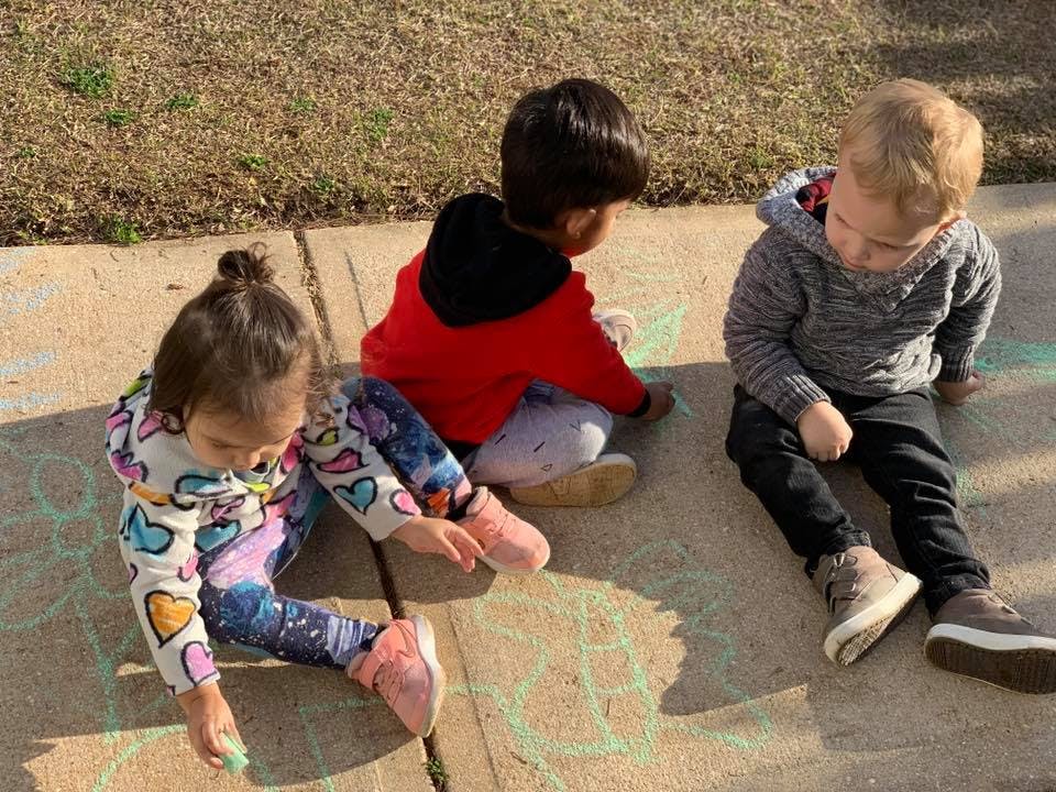 Three children sitting on pavement drawing with chalk