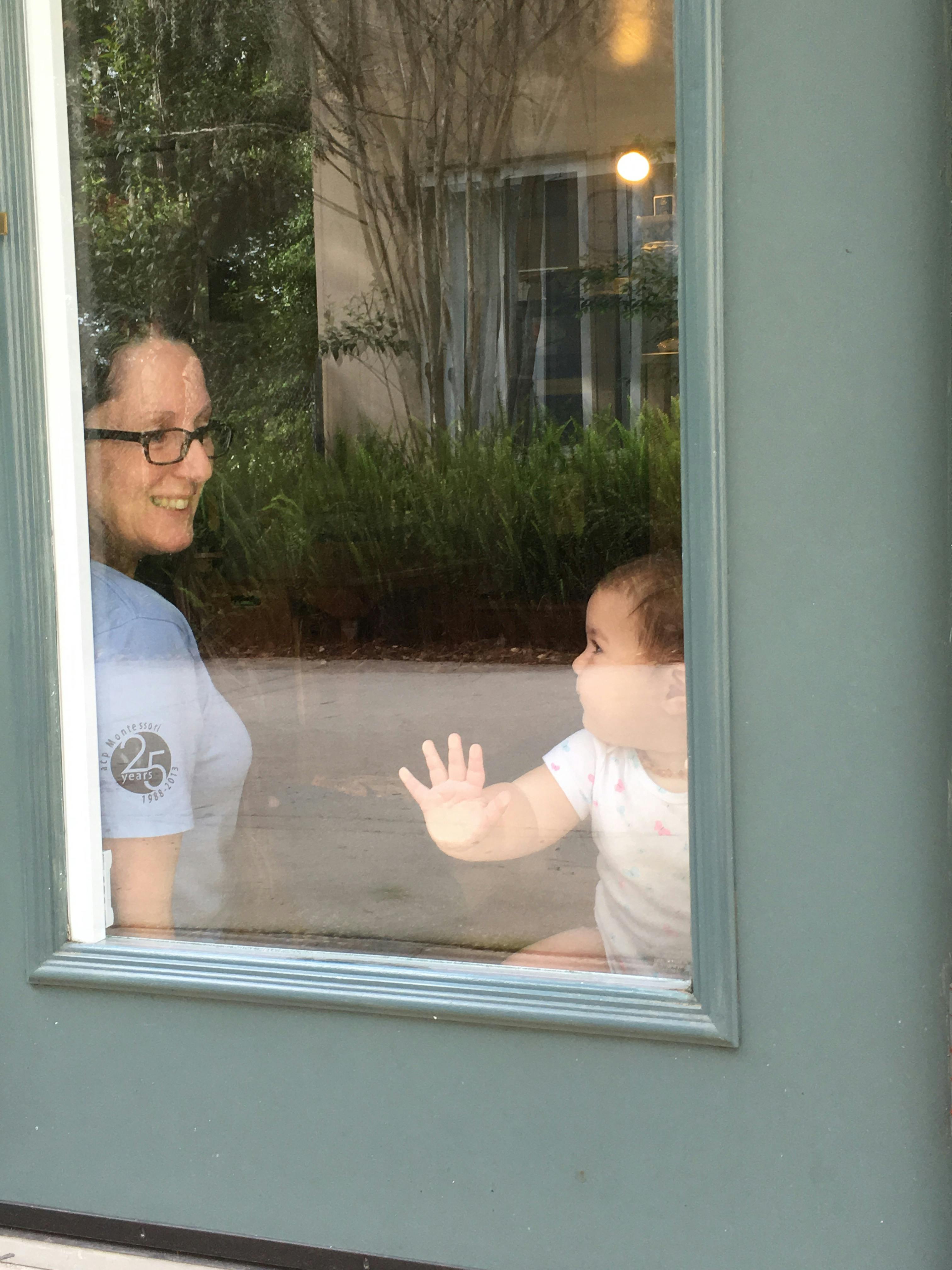 Person in glasses looking at a child with hand on glass
