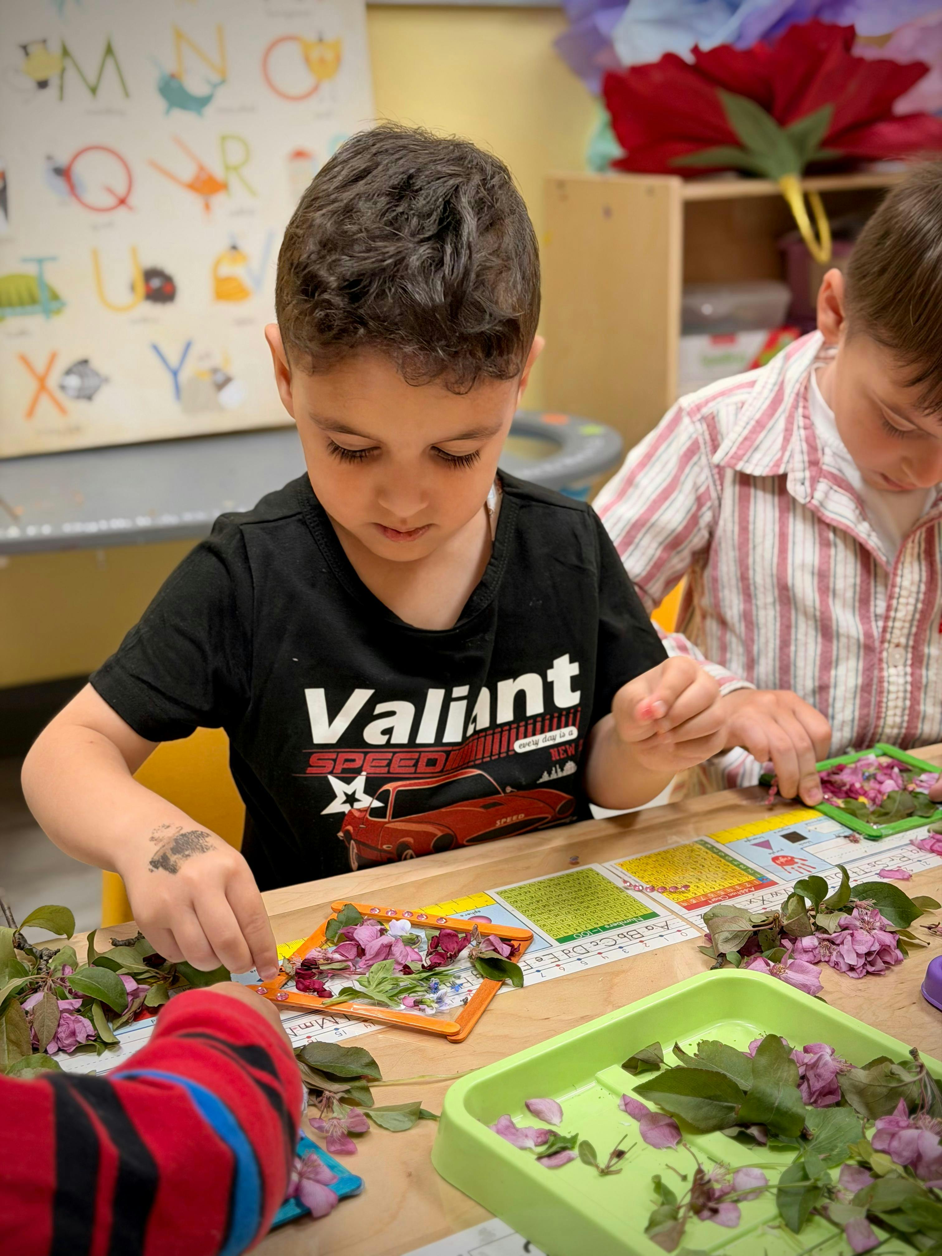 Children arranging leaves and flowers in small frames at a table