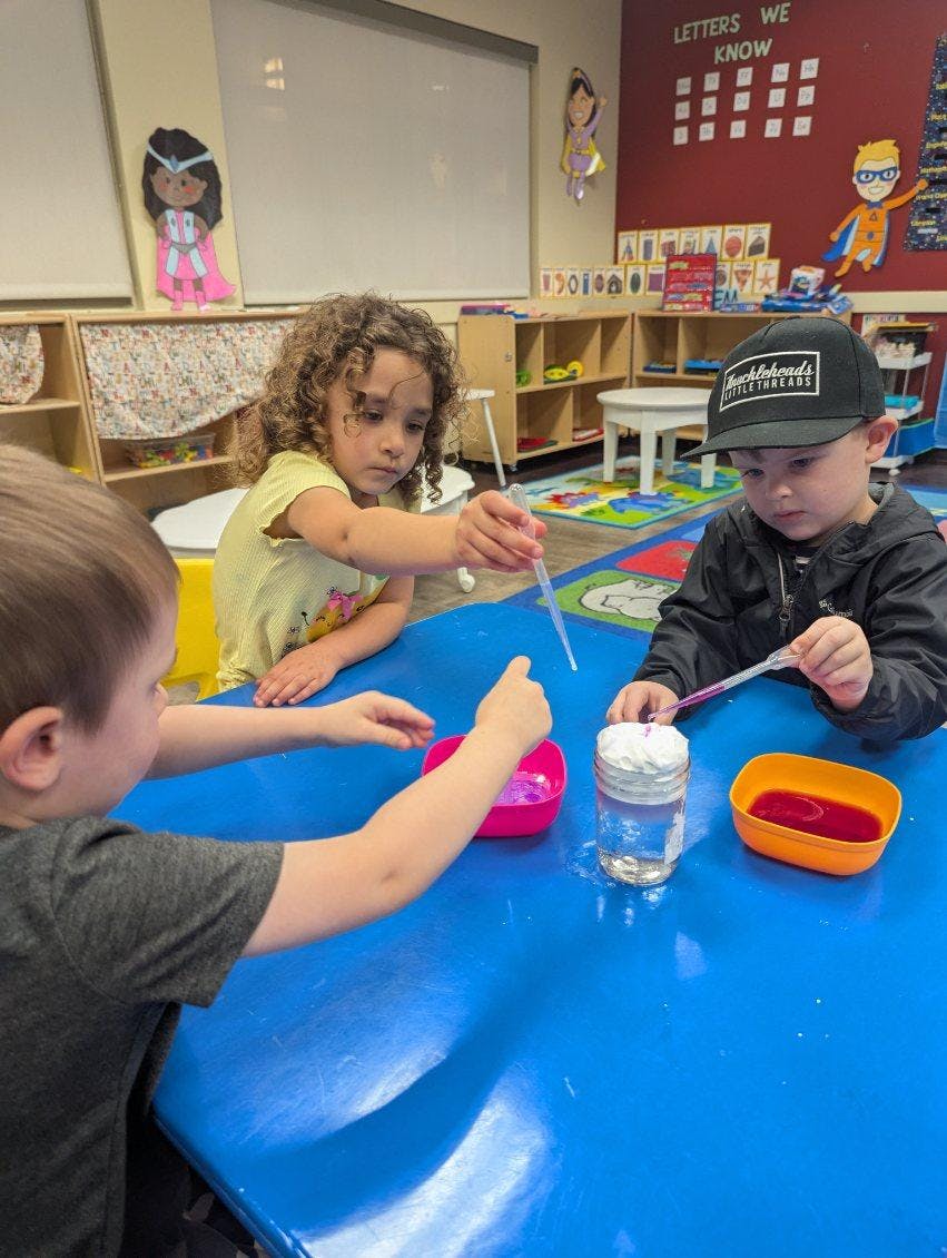 Three children using droppers to experiment with liquid and foam at a table