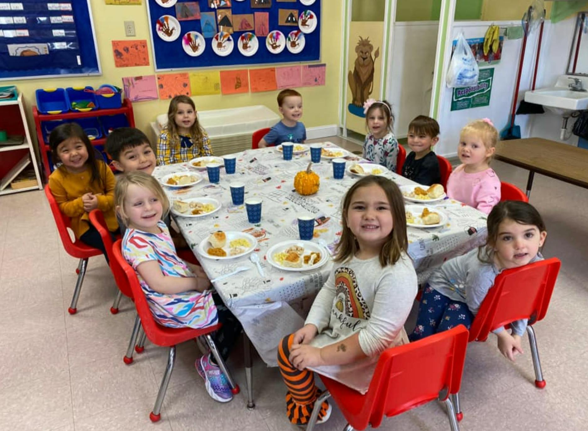 Children sitting around a table with plates of food in a classroom