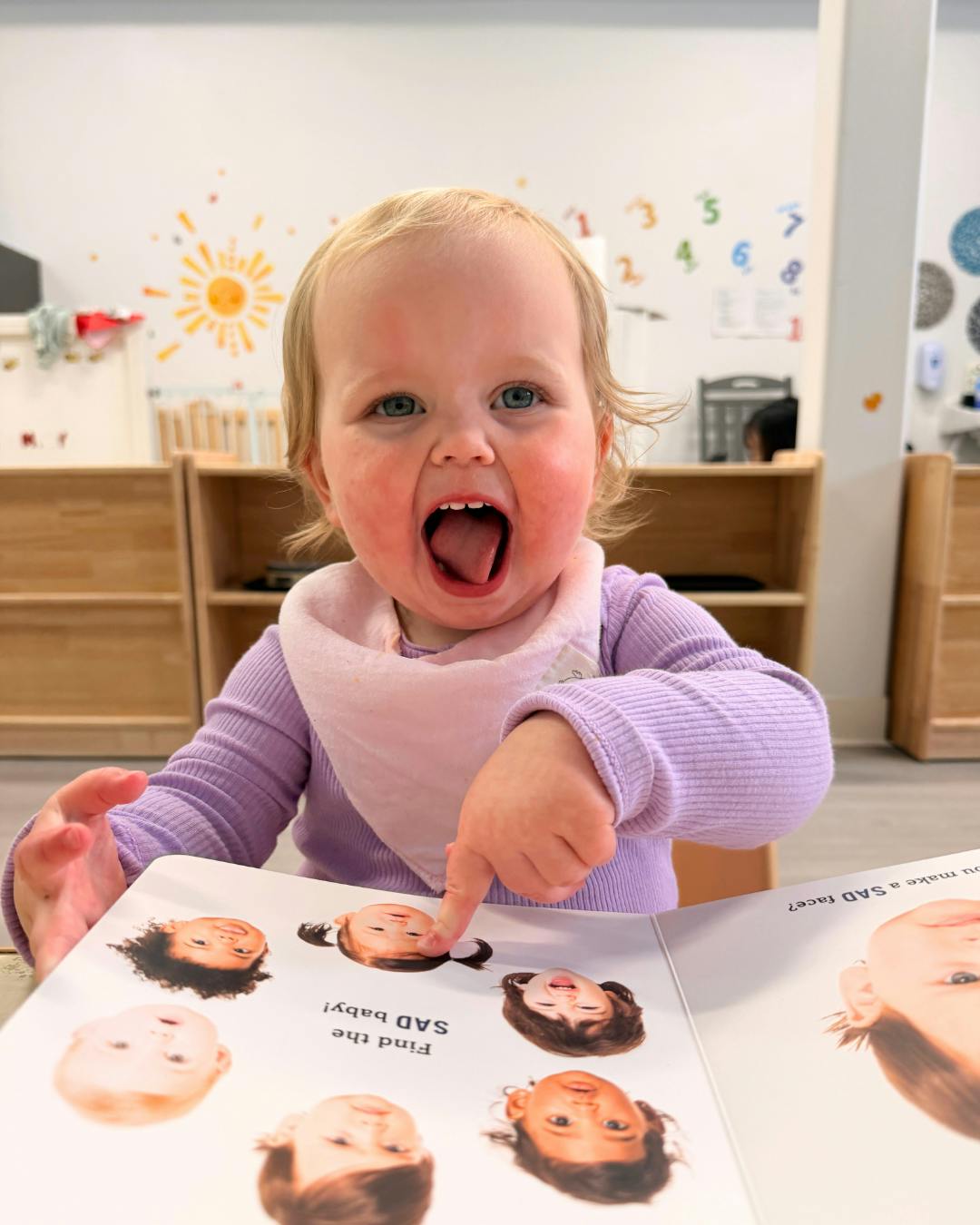 Child pointing at a book with faces while mouth is open