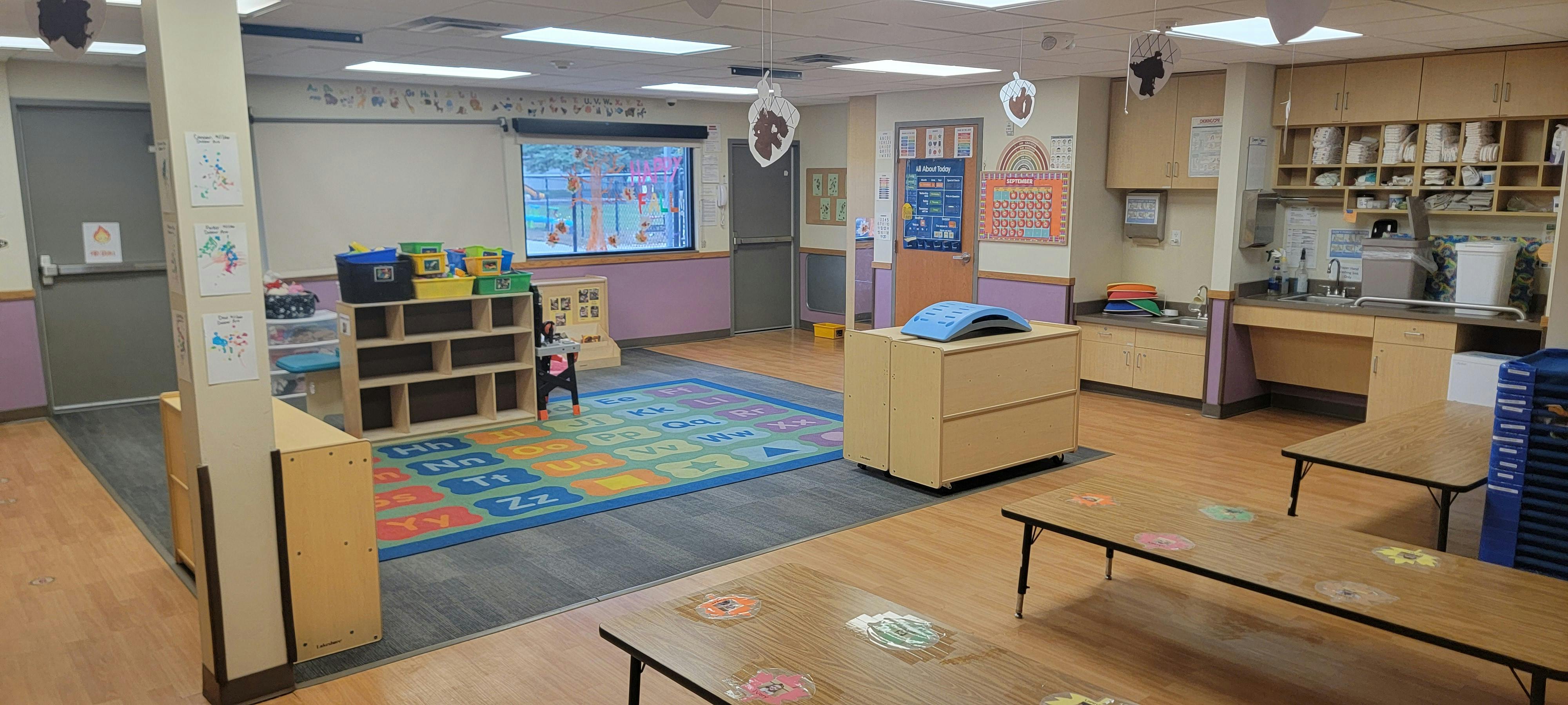 Empty preschool classroom with alphabet rug and wooden furniture