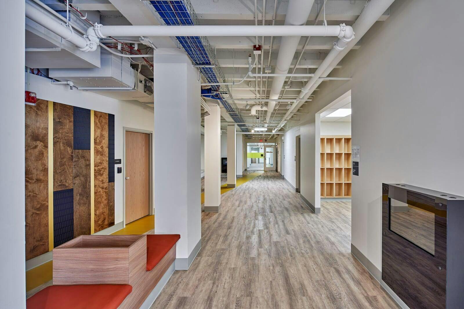 Long hallway with wood-patterned floor and exposed ceiling pipes