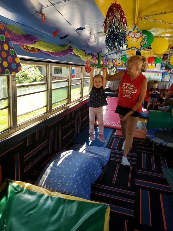 Adult helping a child hang from a bar inside a decorated bus