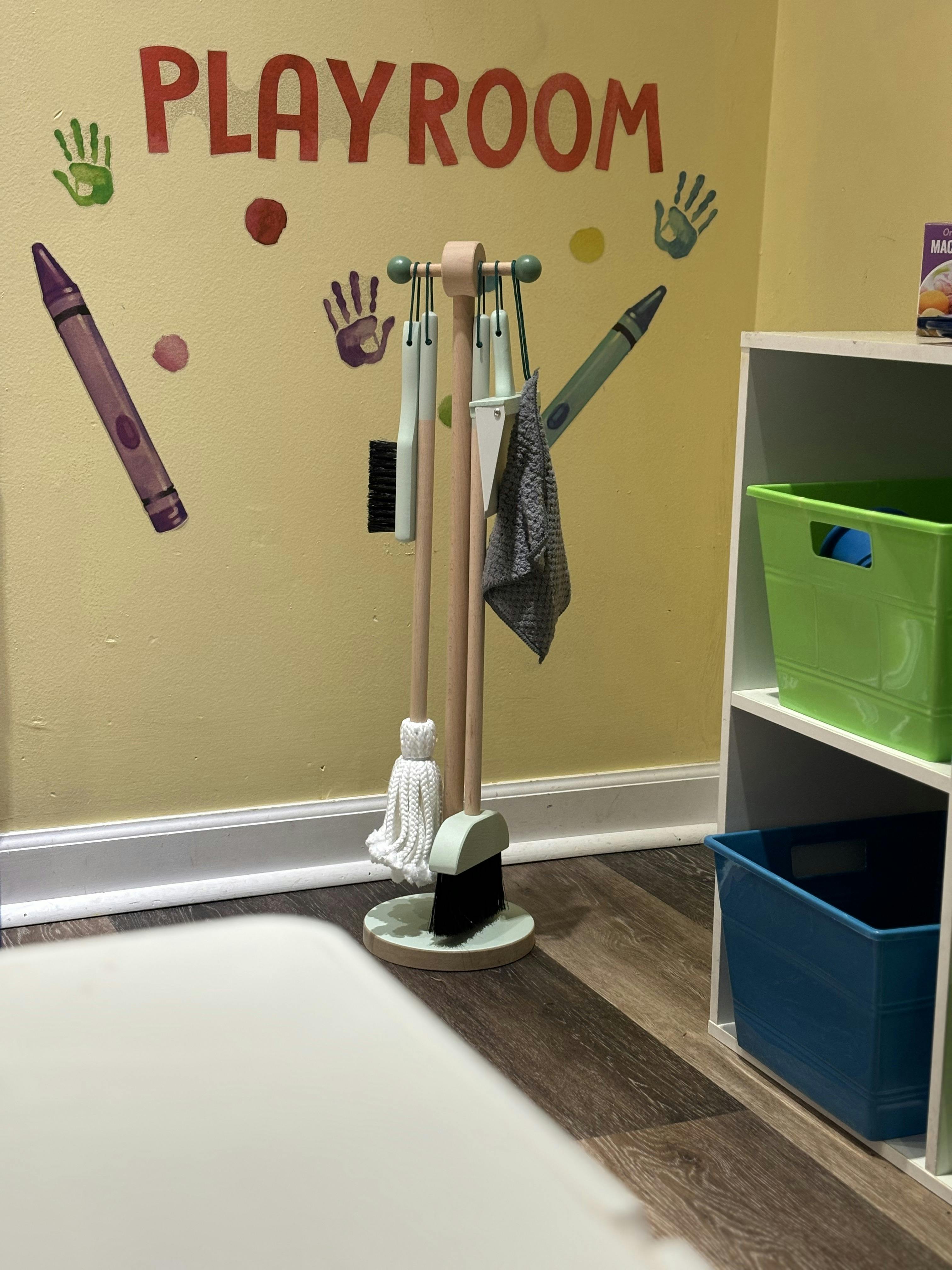 Playroom wall with colorful handprints and crayons, next to a toy cleaning set