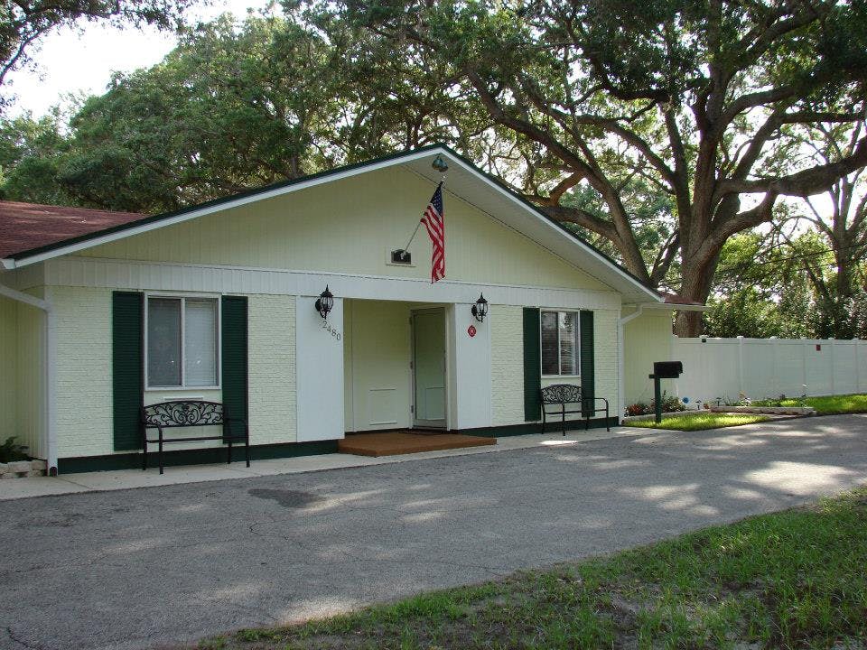 Front of a light-colored building with dark green shutters and an American flag