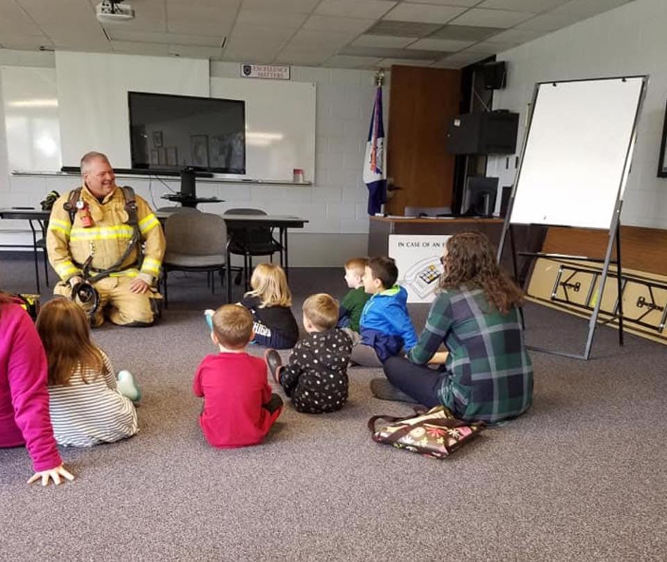 Firefighter kneeling with children and an adult sitting on the floor