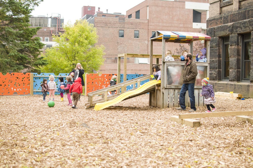 People and children on a playground with a slide and play structure