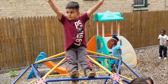 Child standing on a playground climbing dome with arms raised