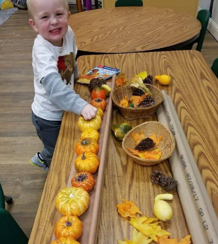 Child playing with small pumpkins on a table