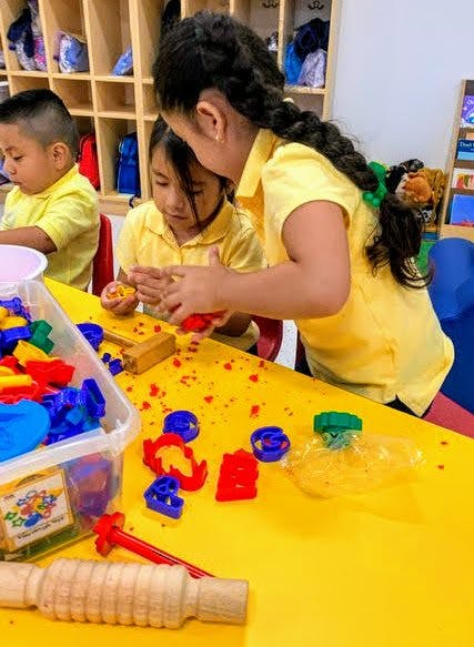 Three children playing with colorful toys at a yellow table