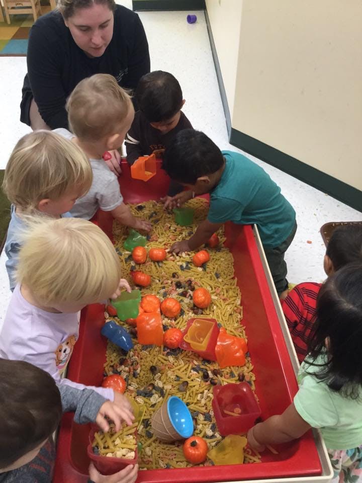 Adult and children playing with sensory bin filled with pasta and small objects