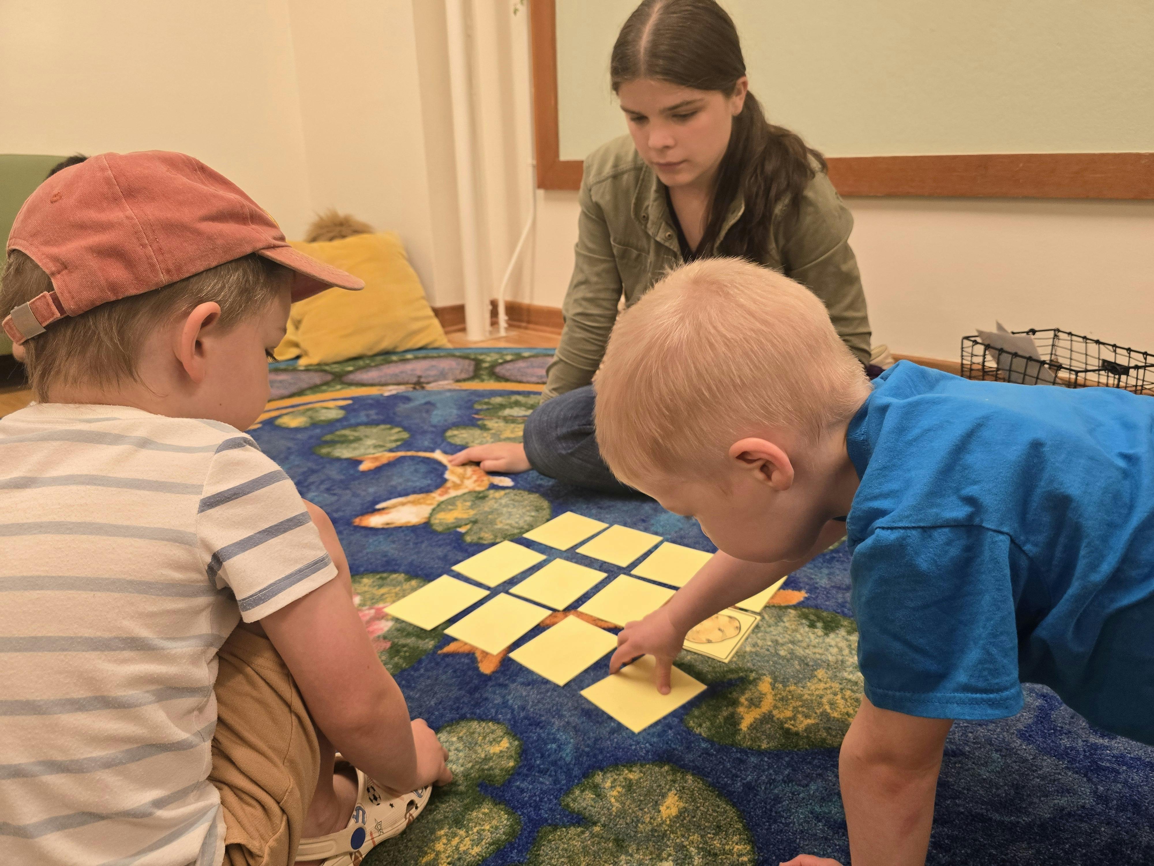 A person and two children playing a game with cards on a floor rug