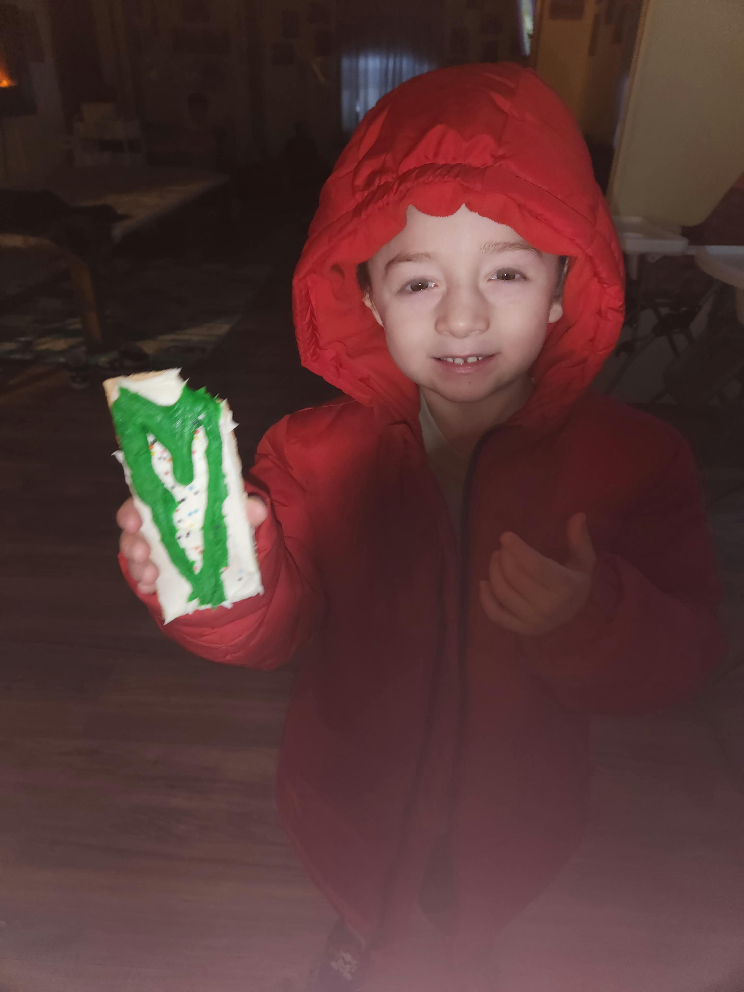 Child in red hooded jacket holding a piece of bread with green frosting