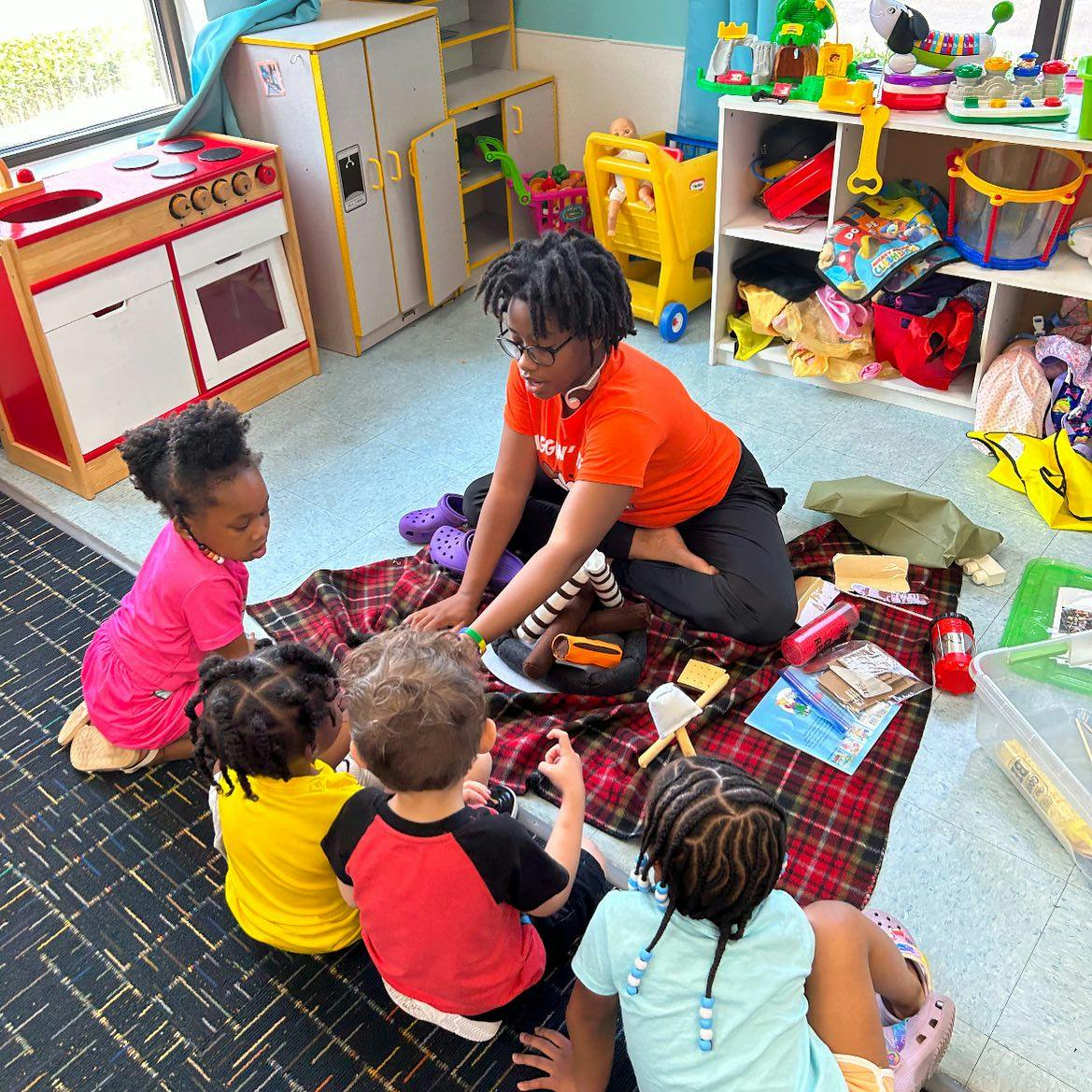 Person and multiple children sitting on a blanket on the floor